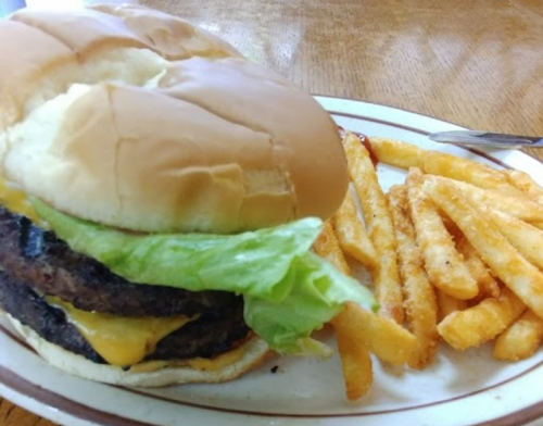 A cheeseburger with lettuce and two patties, served with a side of golden fries on a plate.