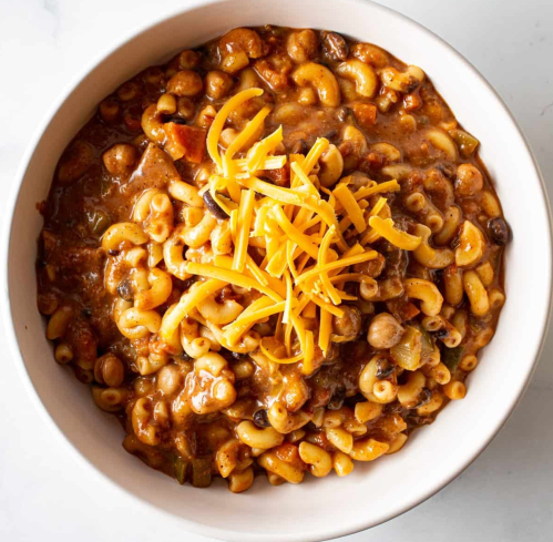 A bowl of macaroni and cheese topped with shredded cheddar, featuring a hearty, savory sauce with vegetables.