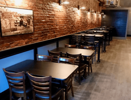 A cozy restaurant interior with brick walls, wooden tables, and chairs arranged in rows under warm lighting.