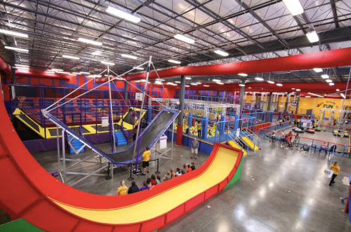 A vibrant indoor trampoline park with various play structures and colorful slides, filled with children and adults enjoying.