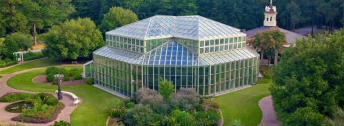 Aerial view of a glass greenhouse surrounded by lush greenery and landscaped gardens.