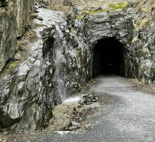 A rocky tunnel entrance with water cascading down the side, leading into a dark passageway.