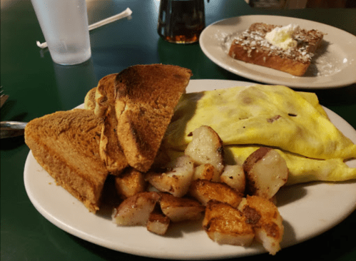 A plate with toast, a yellow omelet, and crispy potatoes, with a side of French toast in the background.