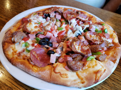 A delicious pizza topped with pepperoni, sausage, ham, olives, green peppers, and tomatoes on a golden crust.