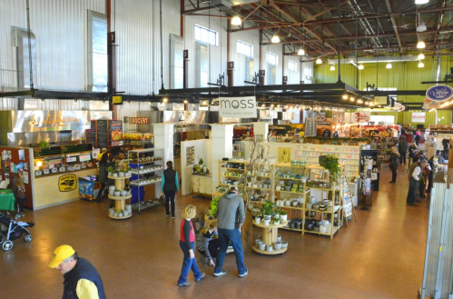 A bustling indoor market with various stalls, shoppers, and vibrant displays of food and goods.