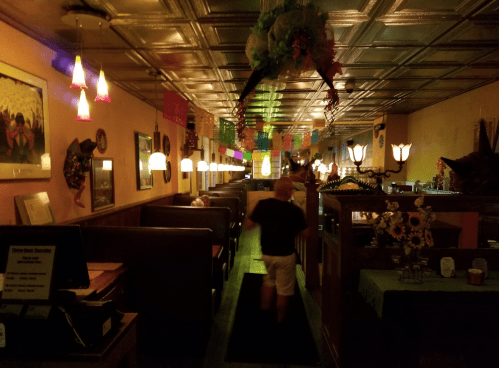 A dimly lit restaurant interior with colorful decorations, booths, and festive lights, creating a warm atmosphere.