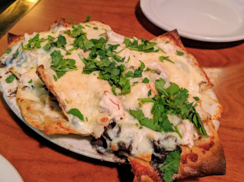 A plate of cheesy nachos topped with shredded chicken and fresh cilantro on a wooden table.