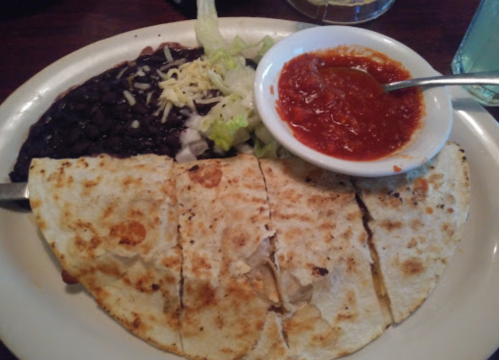 A plate of quesadillas with black beans, lettuce, cheese, and a side of salsa.