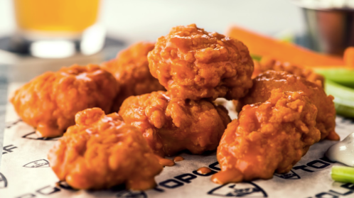 A close-up of crispy, sauced chicken wings on a paper-lined plate, accompanied by celery and carrots.
