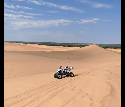 A quad bike parked on sandy dunes under a clear blue sky, with tire tracks leading into the distance.