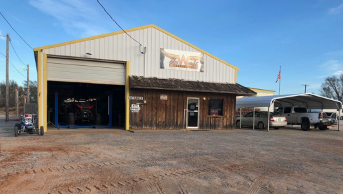 A large yellow and wooden building with a sign, featuring an open garage and parked vehicles outside.