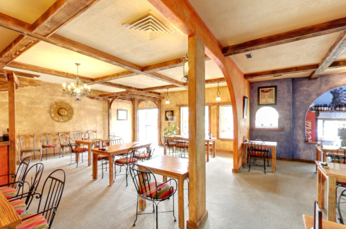 Cozy restaurant interior with wooden beams, tables, and colorful chairs, featuring warm lighting and a welcoming atmosphere.