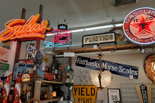 A collection of vintage signs and neon lights, including "Salsa's," "Budweiser," and "Gasoline Filling Station."