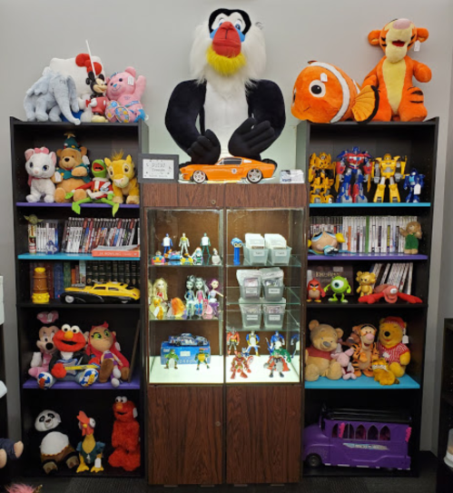 A display of colorful stuffed animals and toys on shelves, with a glass cabinet showcasing action figures and collectibles.