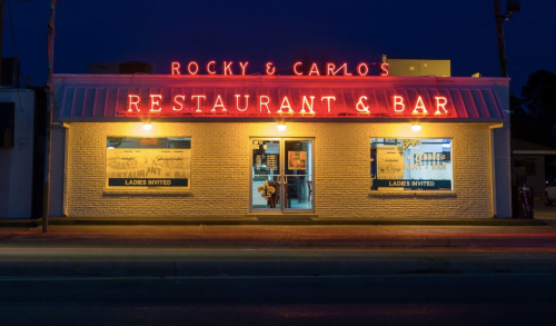 Neon-lit facade of Rocky & Carlo's Restaurant & Bar at night, featuring inviting signage and a welcoming atmosphere.