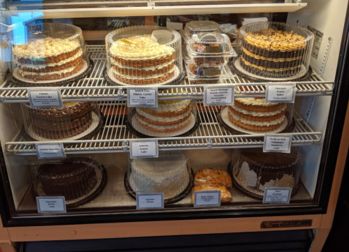 A display case filled with various cakes, each labeled, showcasing different flavors and designs.