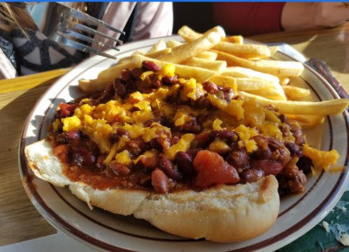 A plate with a chili cheese dog topped with cheddar cheese, served with a side of golden French fries.