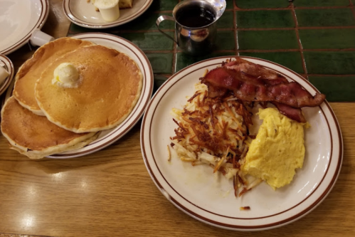 A breakfast plate with pancakes, bacon, scrambled eggs, and hash browns, alongside a cup of coffee.