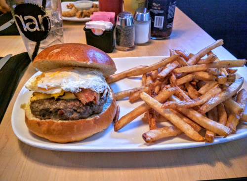 A juicy burger with a fried egg and bacon, served with a side of crispy French fries on a white plate.