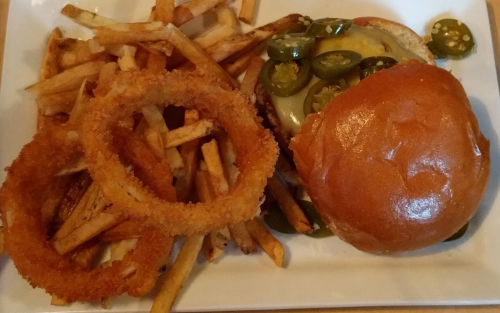 A plate featuring a cheeseburger topped with jalapeños, served with crispy fries and onion rings.
