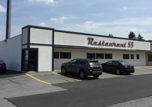 Exterior of Restaurant 55, a white building with a sign, featuring parked cars in front on a sunny day.