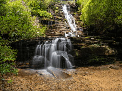A serene waterfall cascading over rocky steps, surrounded by lush greenery and a calm pool at the base.