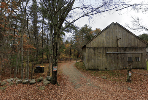 A gravel path leads to a wooden barn surrounded by trees with autumn leaves, creating a serene rural scene.