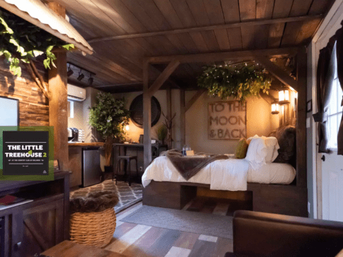 Cozy treehouse interior with a bed, wooden decor, and greenery, featuring a sign that reads "To the Moon & Back."