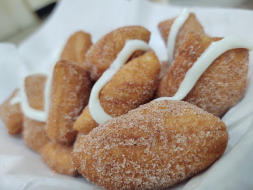 A close-up of golden-brown, sugar-coated pastries drizzled with white icing on a white paper background.