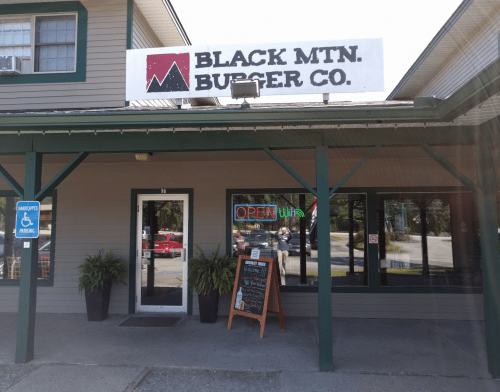 Exterior of Black Mtn. Burger Co. featuring a sign, open neon lights, and a chalkboard menu outside.