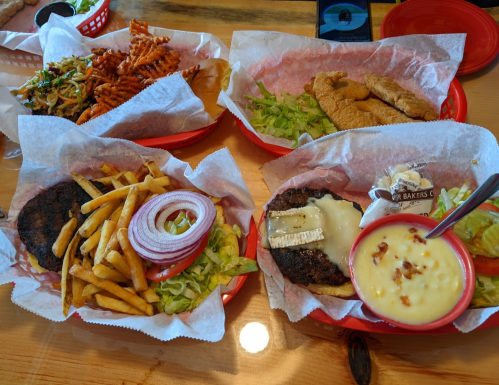 A spread of burgers, fries, and fried fish served in red baskets with lettuce and onion on a wooden table.