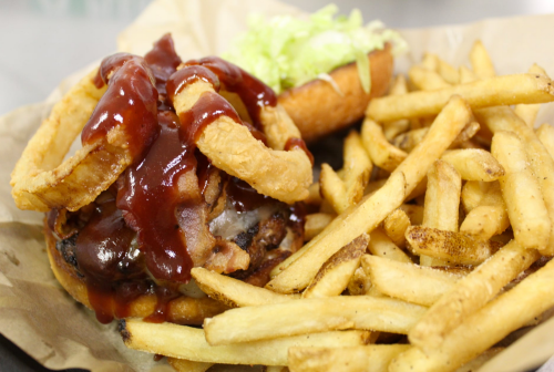 A juicy burger topped with onion rings and barbecue sauce, served with a side of golden fries and a bun with lettuce.