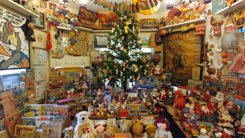 A colorful room filled with vintage toys, decorations, and a Christmas tree surrounded by nostalgic memorabilia.