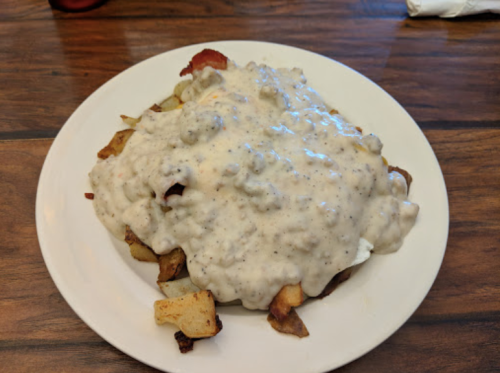 A plate of crispy potatoes topped with creamy sausage gravy and bits of bacon.