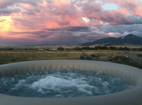 A hot tub with bubbling water, set against a vibrant sunset and mountains in the background.