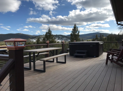 A scenic deck with a hot tub, picnic table, and mountain views under a partly cloudy sky.