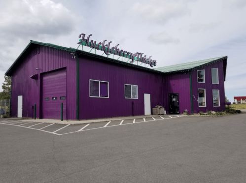A vibrant purple building with a green roof, featuring the sign "Huckleberry Picker" on top.