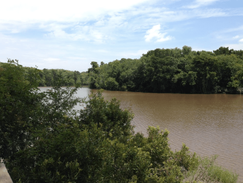 A serene river scene surrounded by lush greenery under a partly cloudy sky.