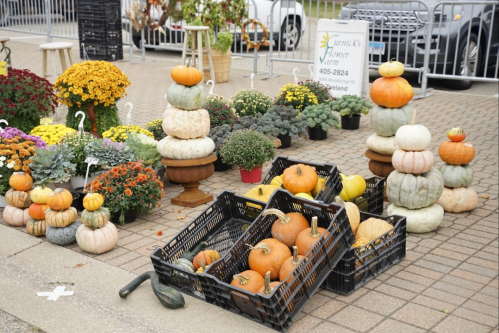 A display of pumpkins and mums at a farm stand, featuring stacked pumpkins and baskets of various gourds.