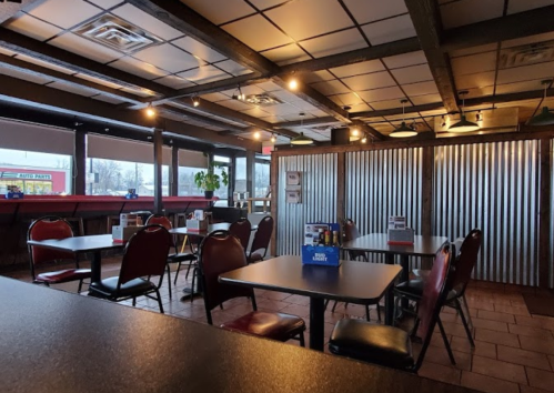 Interior of a casual dining restaurant with empty tables and chairs, large windows, and a metal wall feature.