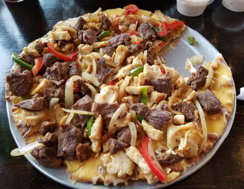 A large pizza topped with grilled chicken, beef, onions, and bell peppers on a cheesy crust.