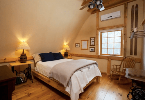 Cozy bedroom with wooden accents, a bed, lamps, a rocking chair, and a large window letting in natural light.