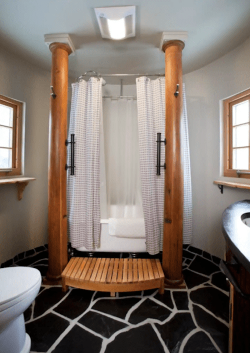 A modern bathroom featuring a shower with wooden columns, a wooden floor, and natural light from windows.
