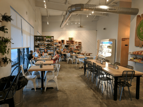 A spacious café with wooden tables, metal chairs, and customers enjoying their meals in a bright, modern setting.