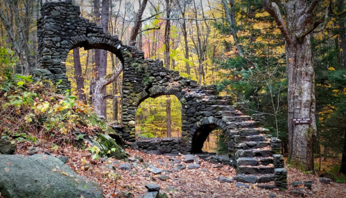 Stone ruins with arches surrounded by autumn foliage in a forest setting.