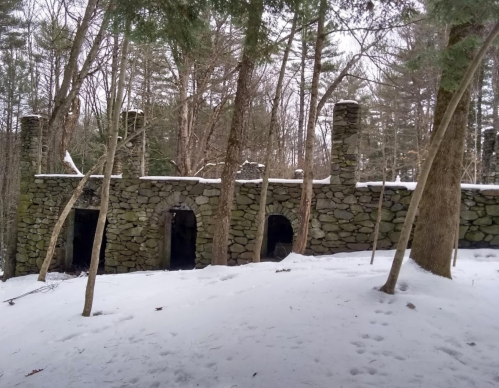 Abandoned stone structure in a snowy forest, surrounded by trees and remnants of a winter landscape.