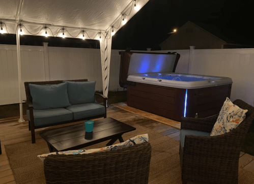 Cozy outdoor seating area with a hot tub, illuminated by string lights, under a tent at night.