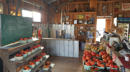A rustic market interior with shelves of tomatoes and bananas, a chalkboard, and vintage decor on wooden walls.