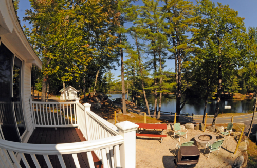 A scenic view from a deck overlooking a calm lake surrounded by trees and a cozy seating area.