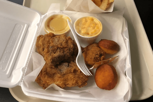 A takeout tray with two pieces of fried chicken, macaroni and cheese, and two cornbread muffins.